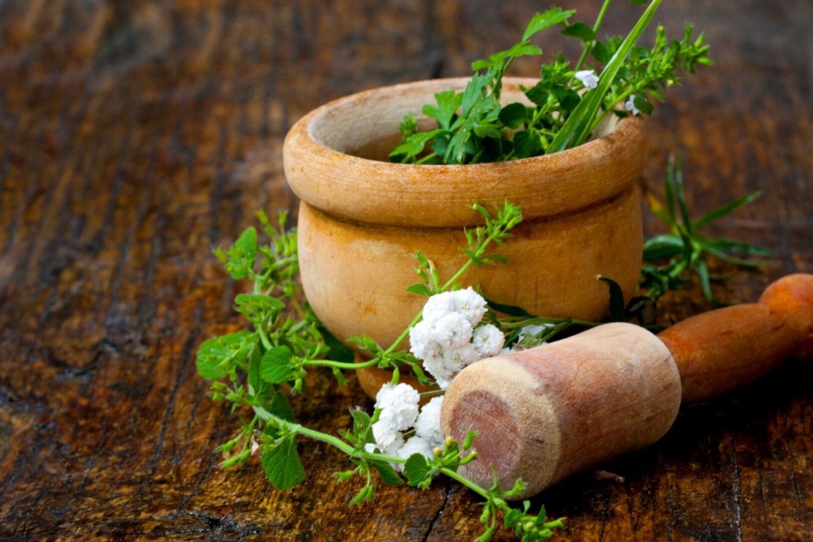 A wooden bowl with herbs and a cork on it.